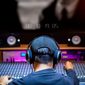 Hombre joven con gorra y cascos sentado frente a un estudio de producción